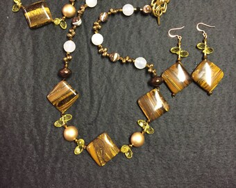 May include: A gold necklace with tiger's eye and white beads, and matching earrings with tiger's eye and gold beads.
