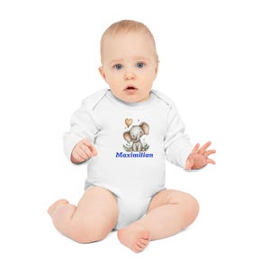 Könnte beinhalten: Weißer Baby-Body mit langen Ärmeln. Der Body zeigt eine Aquarell-Illustration eines grauen Elefanten mit einem herzförmigen Ballon und dem Namen "Maximilian" in blauer Schrift. Das Baby sitzt und schaut in die Kamera.