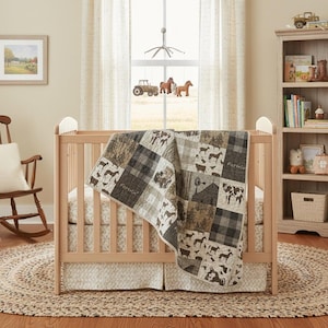May include: A wooden crib with a farm-themed quilt featuring images of horses, cows, and barns. The quilt is draped over the crib, which is set on a round jute rug. A mobile with farm animals hangs above the crib.