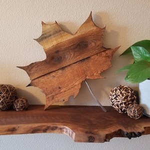 May include: A wooden maple leaf wall decor made from reclaimed wood with a rustic finish. The leaf is mounted on a metal rod and is displayed on a wooden shelf with decorative balls.