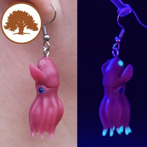 May include: A pair of earrings featuring a small, pink octopus with blue eyes. The octopus glows in the dark, with the tentacles and eyes glowing a bright blue.