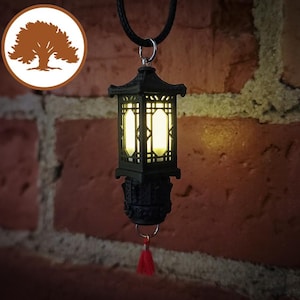 Pode incluir: Um pingente de lanterna preta com uma borla vermelha pendurada em uma parede de tijolo. A lanterna tem uma luz dentro e um design decorativo.