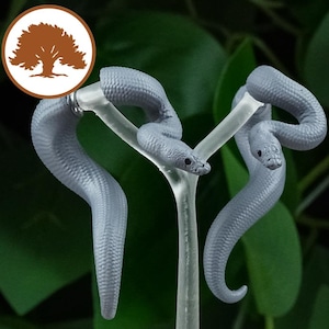 May include: Two gray snake-shaped earrings with a textured surface. The earrings are hanging from a clear plastic stand.