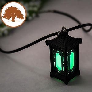 Puede incluir: Un collar de cadena negro con un dije de linterna verde brillante. La linterna tiene un diseño detallado y un estilo chino tradicional.