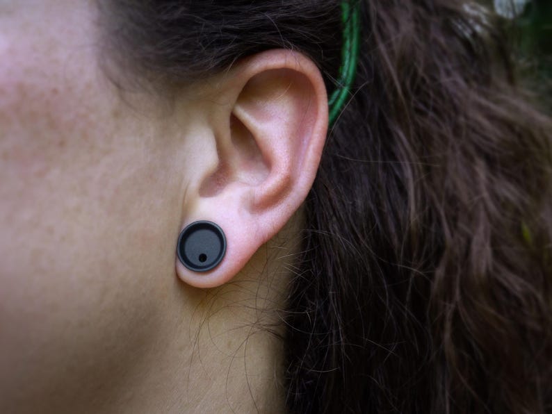 May include: A person with long dark hair wearing a black ear gauge in their left ear.