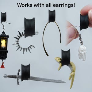 May include: Black silicone earring backs that can be used with a variety of earrings. The backs are shown holding a variety of earrings, including a lantern, a sword, a ring, a thin wire earring, and a small white figurine.