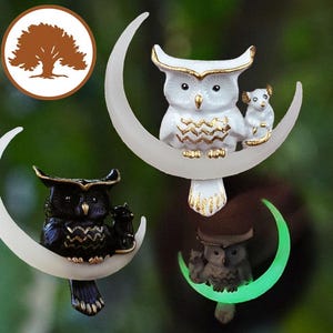 May include: Three ceramic owl figurines perched on crescent moon shapes. The owls are white with gold accents, black with gold accents, and green with gold accents. The moons are white, white, and glow-in-the-dark green.