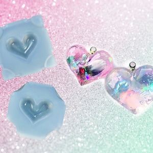 May include: Two silicone heart-shaped molds and two iridescent resin heart-shaped pendants with a holographic finish. The molds are light blue and the pendants are pink and blue.