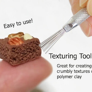 May include: A close-up of a small, brown chocolate cake with white and brown toppings. A hand holds a texturing tool with a silver handle and multiple thin metal prongs. The text "Texturing Tool" is written below the tool, and the text "Great for creating crumbly textures on polymer clay" is written below that. The text "Easy to use!" is written above the cake.