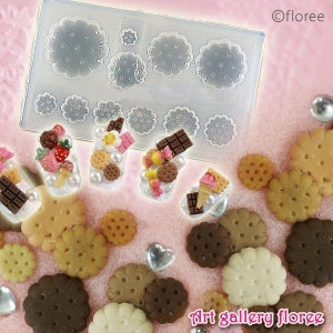 Pu&ograve; includere: Uno stampo in plastica trasparente con pi&ugrave; forme rotonde per fare biscotti. Lo stampo &egrave; su una superficie rosa con diversi piccoli biscotti decorati. I biscotti sono decorati con cioccolato, codette e altri condimenti. Il testo "Art gallery floree" &egrave; visibile nell'angolo in basso a destra dell'immagine.