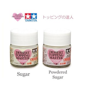 May include: Two small white bottles of Tamiya Dessert Topping Master paint, one labeled "Sugar" and the other "Powdered Sugar". The bottles are part of the Tamiya Decoration Series.