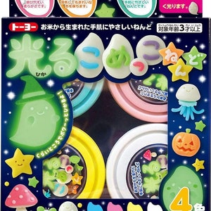 Puede incluir: Un paquete de plastilina que brilla en la oscuridad con cuatro colores: azul, rosa, amarillo y blanco. El paquete incluye el texto "トーヨー" y "お米から生まれた手肌にやさしいねんど" que se traduce como "Toyoo" y "Plastilina a base de arroz, suave para la piel".