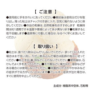 May include: A white, clay-like substance in a container with a white lid. The container has a black and white label with the text "[ご注意]" and "[取り扱い]" in Japanese. The label also includes instructions for using and storing the clay. The main ingredient is listed as "樹脂系中空体、石粉等" in Japanese.