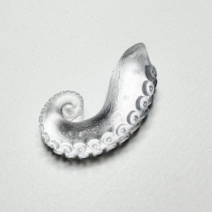 May include: A clear glass octopus tentacle sculpture with a curled shape. The tentacle has a detailed texture and multiple suction cups.