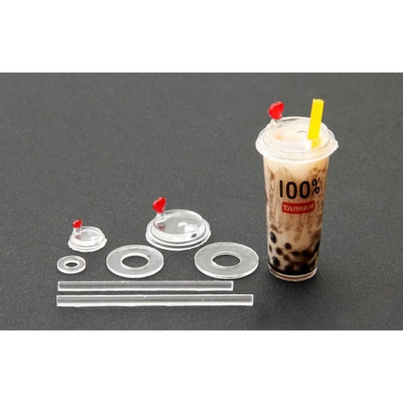 May include: A set of clear plastic lids for bubble tea cups, including a straw, and a cup with a lid and a red and yellow straw. The cup has the text "100% Taiwan" printed on it.