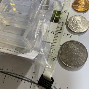 Puede incluir: Un molde de pl&aacute;stico transparente para hacer manualidades de resina. El molde tiene la forma del n&uacute;mero "8" y mide aproximadamente 2,5 cm. El molde se muestra junto a una regla, una moneda de 25 centavos de d&oacute;lar estadounidense y un centavo de d&oacute;lar estadounidense.