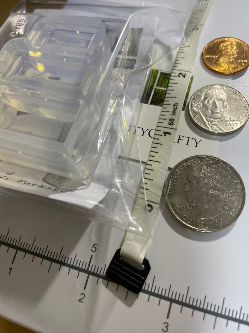 Puede incluir: Un molde de pl&aacute;stico transparente para hacer manualidades de resina. El molde tiene la forma del n&uacute;mero "8" y mide aproximadamente 2,5 cm. El molde se muestra junto a una regla, una moneda de 25 centavos de d&oacute;lar estadounidense y un centavo de d&oacute;lar estadounidense.