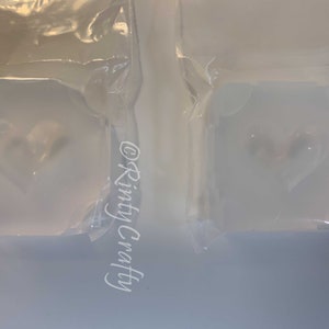 May include: Two clear plastic bags containing white heart-shaped soap bars. The soap bars are in a clear plastic mold. The text "@Rinty Crafty" is visible on the left bag.