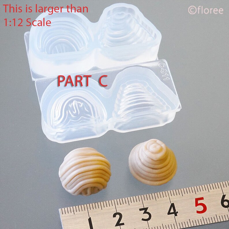 May include: Two silicone moulds for making miniature pastries, one with a swirl design and the other with a cone shape. The moulds are labelled "PART C" and "C-811". Two finished pastries are shown next to a ruler, measuring approximately 2.5 cm in diameter.