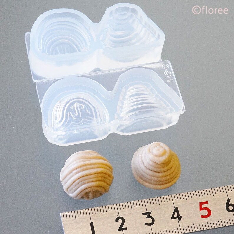 May include: Two clear silicone moulds for making small cake pops. The moulds are divided into two sections, each with a different design. The moulds are shown next to two finished cake pops, one round and one cone-shaped.