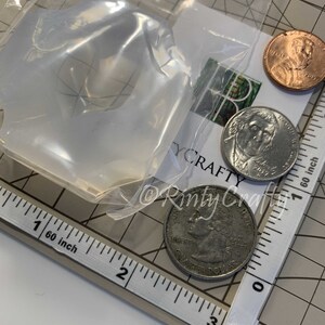 May include: A clear plastic bag containing a silicone mold for making resin crafts. The mold is next to a ruler and three US coins, including a quarter, a dime, and a penny.