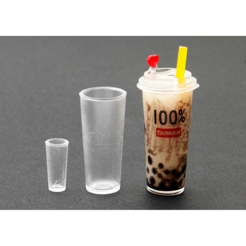 May include: Three clear plastic cups, one with a brown and black beverage with tapioca pearls and a red and yellow straw. The beverage cup has a white label with the text "100% TAIWAN".