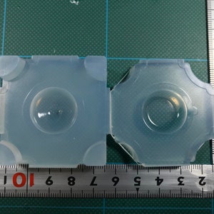 May include: Two clear silicone molds for making resin crafts. The molds are square and round, and are sitting on a green cutting mat with a ruler.