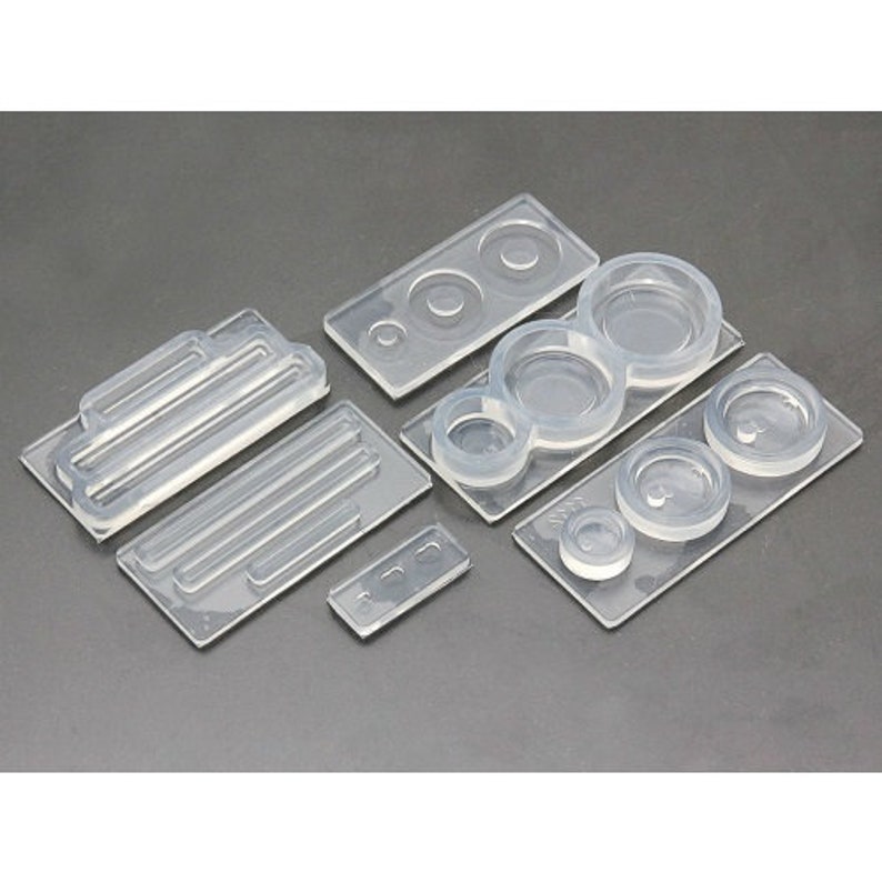 May include: A set of clear silicone molds for crafting. The molds feature various shapes, including circles, ovals, and a rectangular mold with lines.