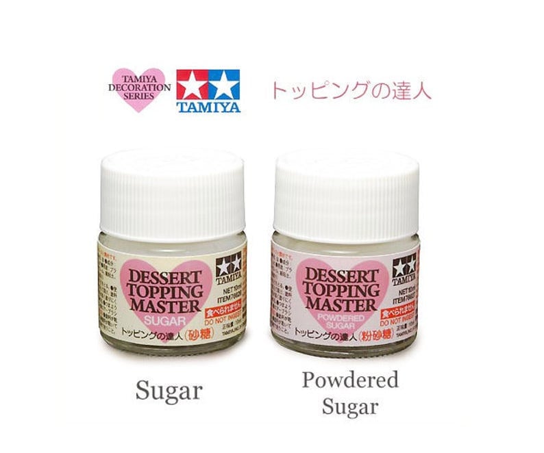 May include: Two small white bottles of Tamiya Dessert Topping Master paint, one labeled "Sugar" and the other "Powdered Sugar". The bottles are part of the Tamiya Decoration Series.