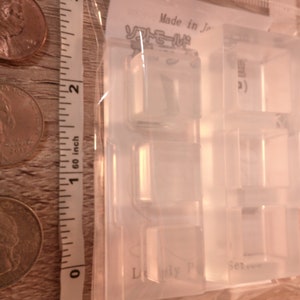 May include: Clear plastic mold for making small, square-shaped resin crafts. The mold has four sections, each with a different design. The mold is labeled "Made in Japan" and "Lovely Polymer Clay Set".