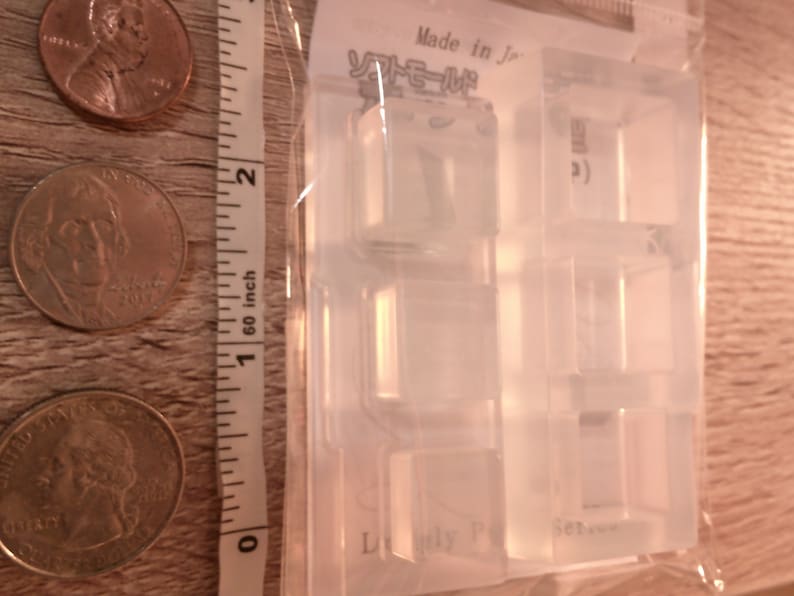 May include: Clear plastic mold for making small, square-shaped resin crafts. The mold has four sections, each with a different design. The mold is labeled "Made in Japan" and "Lovely Polymer Clay Set".
