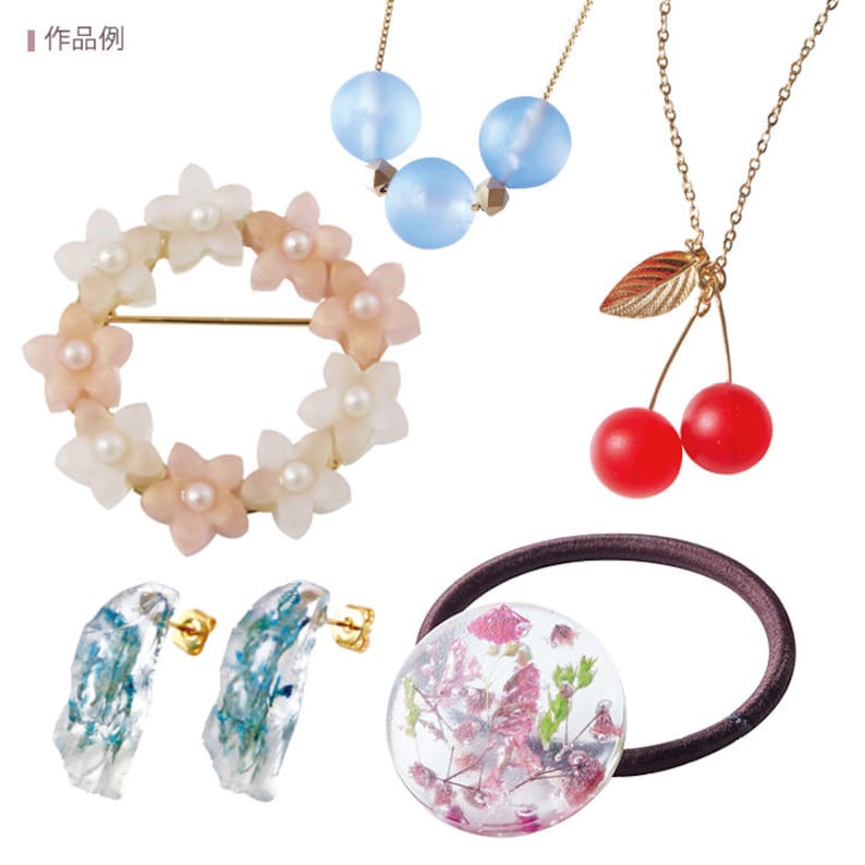May include: A collection of delicate jewelry and accessories. Includes a floral brooch, a three-bead necklace, a cherry pendant necklace, earrings with blue accents, and a hair tie with dried flowers encased in resin.