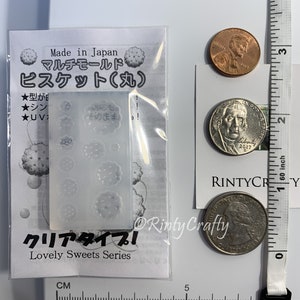 Pu&ograve; includere: Uno stampo in plastica trasparente con otto forme diverse di biscotti. Lo stampo &egrave; etichettato "Multi-Mold Biscuit (Round)" e "Lovely Sweets Series" in giapponese e inglese. Lo stampo &egrave; su uno sfondo bianco con un righello e monete per la scala.