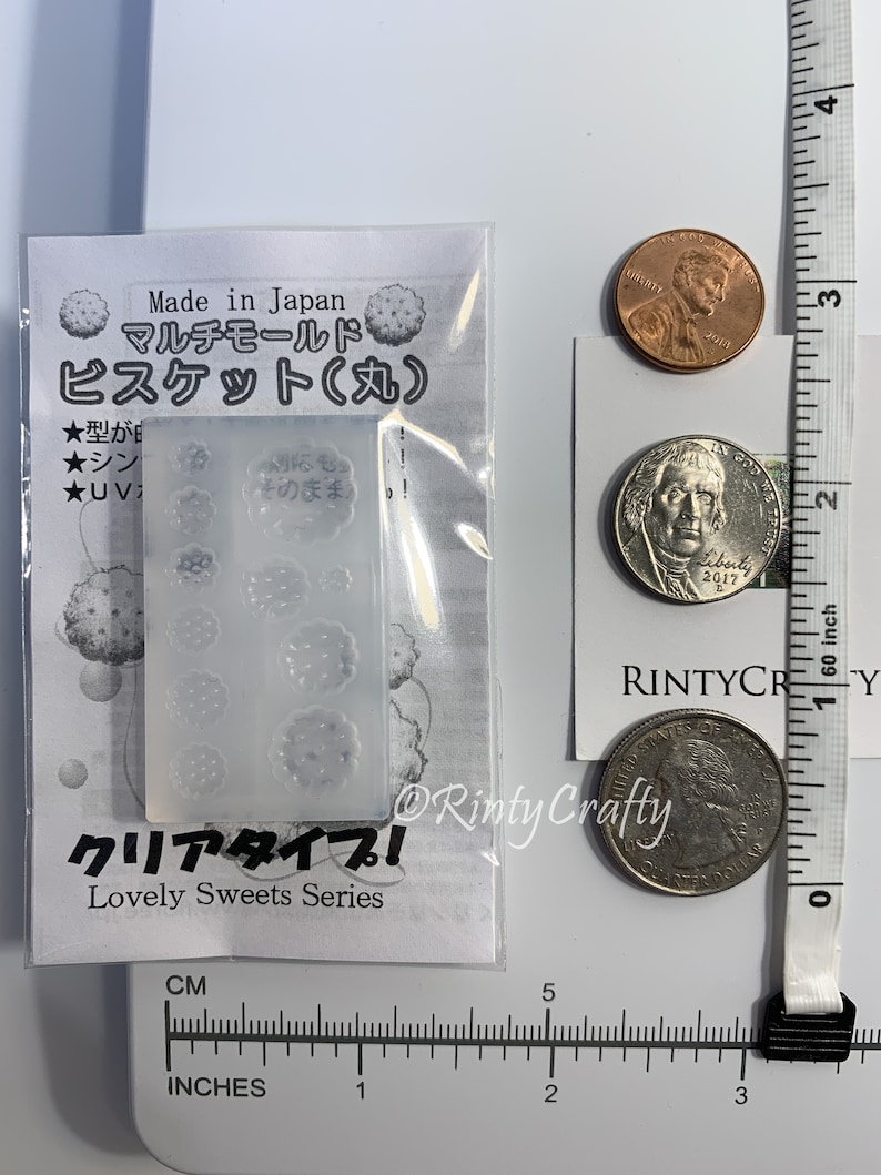 Pu&ograve; includere: Uno stampo in plastica trasparente con otto forme diverse di biscotti. Lo stampo &egrave; etichettato "Multi-Mold Biscuit (Round)" e "Lovely Sweets Series" in giapponese e inglese. Lo stampo &egrave; su uno sfondo bianco con un righello e monete per la scala.