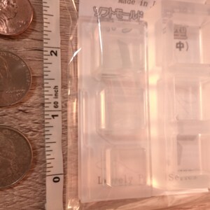 May include: Clear plastic mold with four square cavities for making resin crafts. The mold has the text "Lovely" and "Series" printed on it. The mold is packaged in a clear plastic bag.