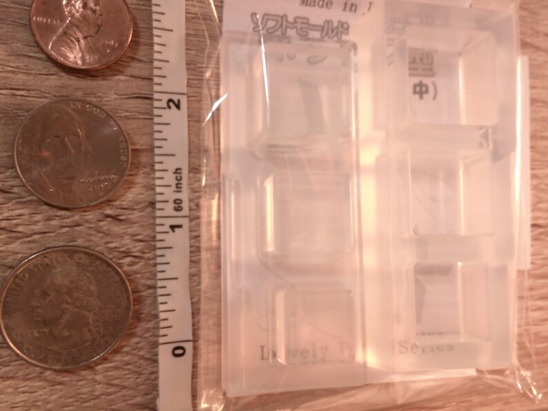 May include: Clear plastic mold with four square cavities for making resin crafts. The mold has the text "Lovely" and "Series" printed on it. The mold is packaged in a clear plastic bag.