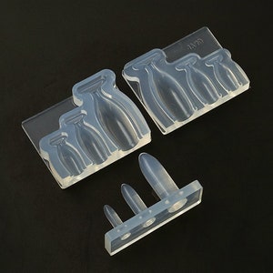 May include: A set of clear silicone moulds for making resin crafts. The moulds are shaped like bottles of various sizes. The moulds are on a black background.