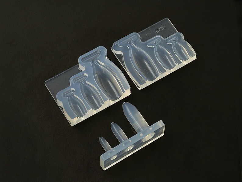 May include: A set of clear silicone moulds for making resin crafts. The moulds are shaped like bottles of various sizes. The moulds are on a black background.