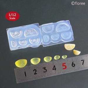 May include: A clear silicone mould with eight different shapes of lemon slices. The mould is 1/12 scale. There are also several small yellow lemon slices next to a ruler.