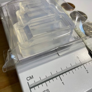 Puede incluir: Un molde de silicona transparente con tres cavidades rectangulares. El molde est&aacute; sobre una regla blanca con marcas en pulgadas y cent&iacute;metros.