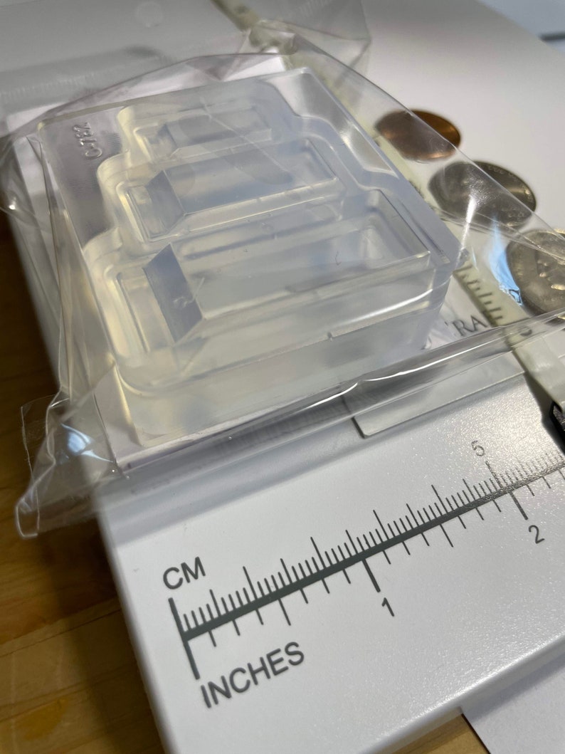Puede incluir: Un molde de silicona transparente con tres cavidades rectangulares. El molde est&aacute; sobre una regla blanca con marcas en pulgadas y cent&iacute;metros.