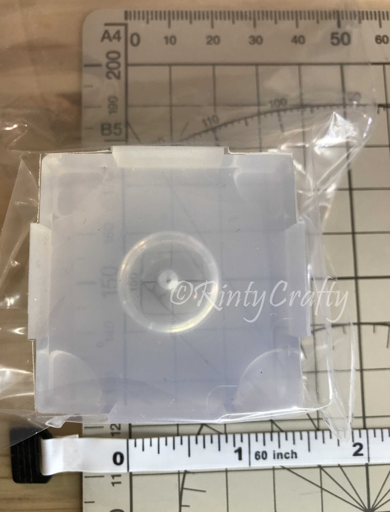 May include: A clear silicone mold for resin casting, featuring a round, recessed area in the center. The mold is approximately 1 inch in diameter.