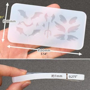May include: A clear silicone mold with various wing and bat designs, including a trident. The mold is rectangular, measuring approximately 3.54 inches long, 1.81 inches wide, and 0.275 inches thick. The designs are for crafting.