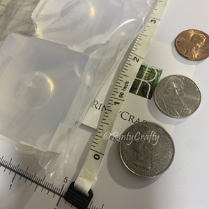 May include: Two clear silicone molds for resin casting, shown with US coins for size comparison. The molds are approximately 1 inch in diameter.