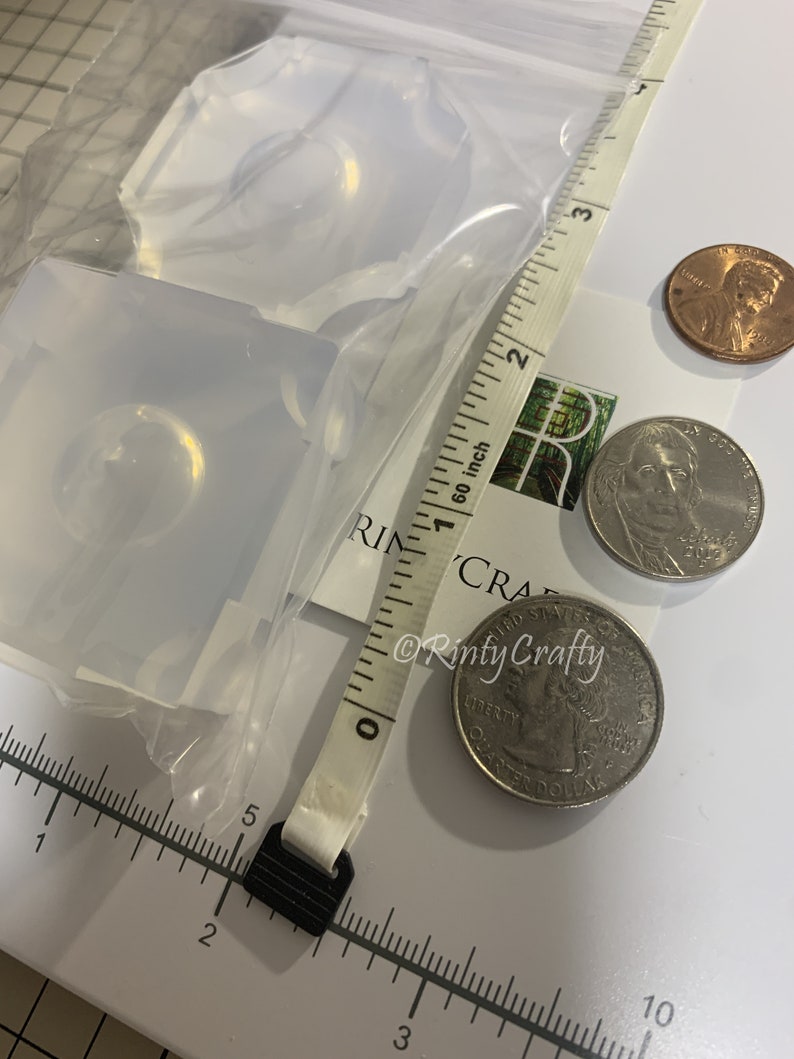 May include: Two clear silicone molds for resin casting, shown with US coins for size comparison. The molds are approximately 1 inch in diameter.