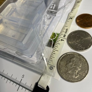 Puede incluir: Un molde de pl&aacute;stico transparente con dos compartimentos rectangulares. El molde est&aacute; sobre una superficie blanca con una regla y dos monedas estadounidenses. La regla est&aacute; marcada en pulgadas y las monedas son una moneda de veinticinco centavos y un centavo.