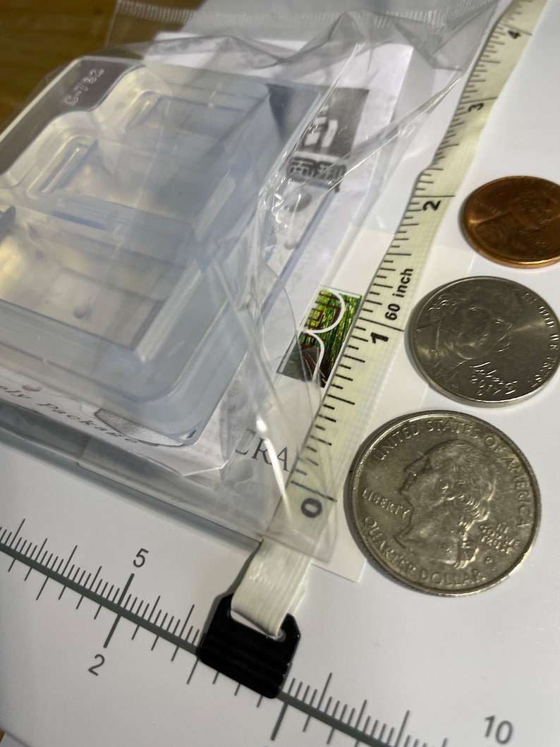 Puede incluir: Un molde de pl&aacute;stico transparente con dos compartimentos rectangulares. El molde est&aacute; sobre una superficie blanca con una regla y dos monedas estadounidenses. La regla est&aacute; marcada en pulgadas y las monedas son una moneda de veinticinco centavos y un centavo.