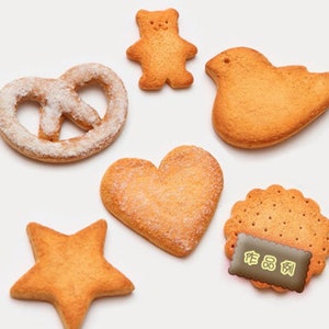 May include: Assortment of six different shaped sugar cookies, including a heart, a star, a pretzel, a bird, a bear, and a round cookie with a textured surface. The cookies are all a light brown color and have a slightly sugary glaze.