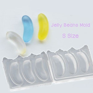 Könnte beinhalten: Eine transparente Silikonform zum Herstellen von Gummibärchen in Form von Jelly Beans. Die Form hat sechs Vertiefungen und ist mit "Jelly Beans Mold S Size" beschriftet. Drei Jelly Beans sind auf dem Bild zu sehen: ein transparentes, ein blaues und ein gelbes.