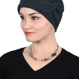 Pode incluir: Um gorro de l&atilde; verde escuro com um design de folhas. O gorro &eacute; usado por uma pessoa com um colar de contas verdes, roxas e pretas.